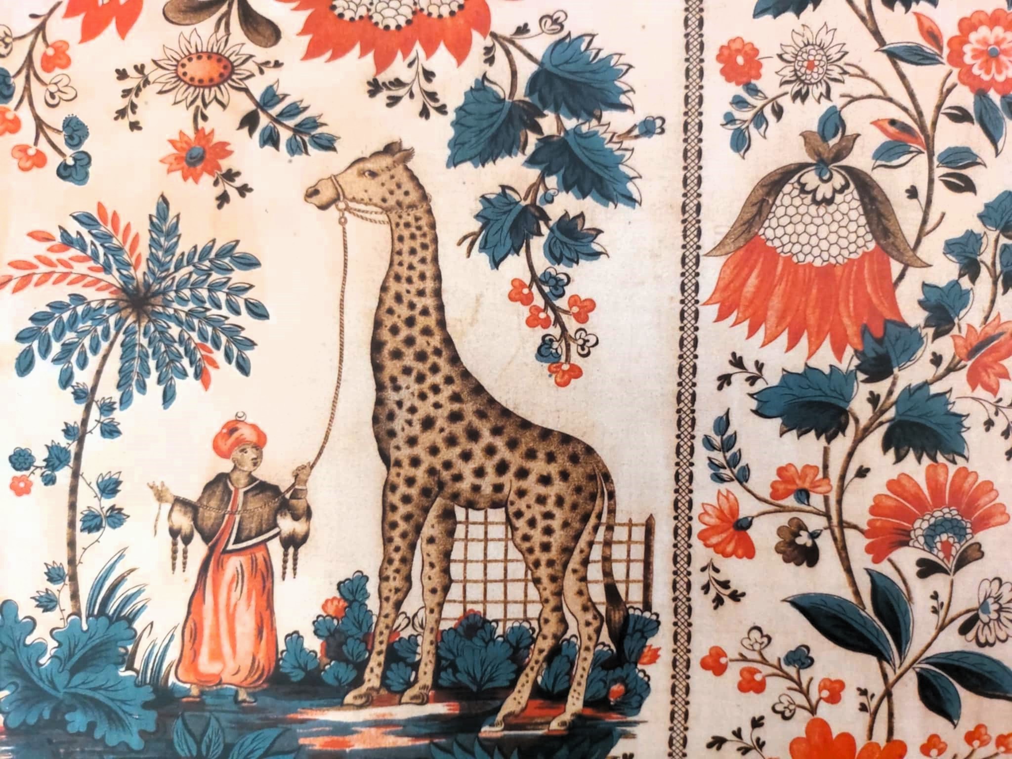 Une tapisserie avec un homme tenant en laisse une girafe, des fleurs et feuilles.